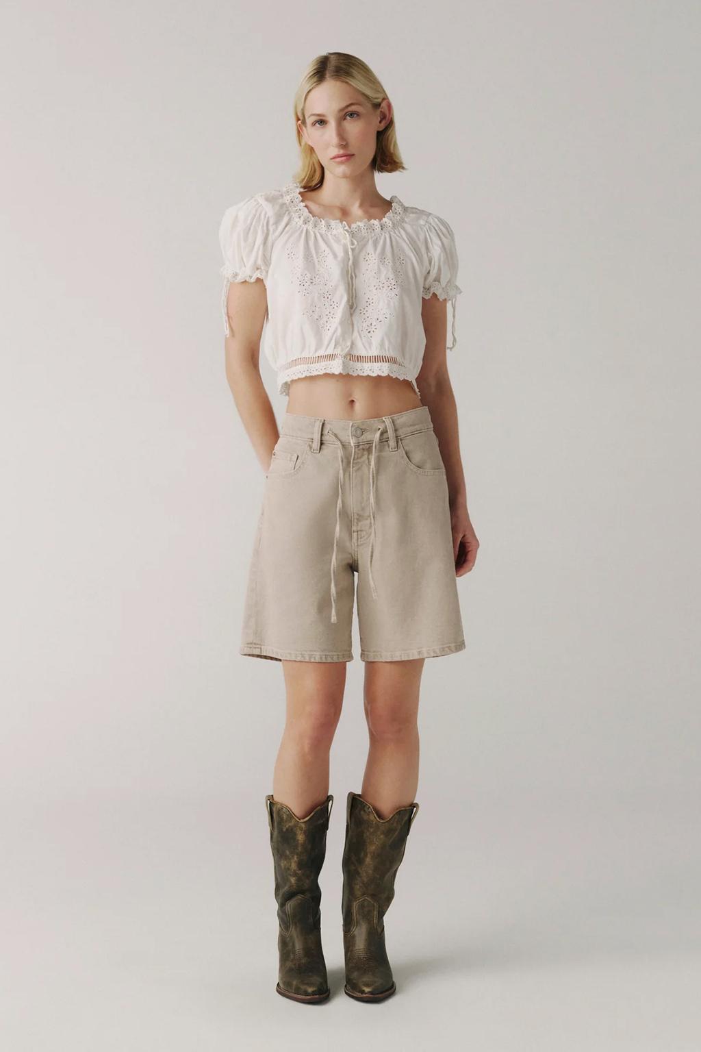 White eyelet crop blouse with beige drawstring shorts and cowboy boots